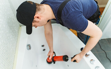 Plumber unclogging bathtub with professional force pump cleaner.