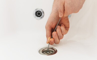 Plumber using drain snake to unclog bathtub. - obrazy, fototapety, plakaty