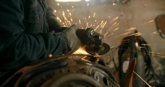 Locksmith sands the metal construction by electric grinder with a lot of sparks in slow motion, metalwork at workshop, 4k 60p Prores HQ
