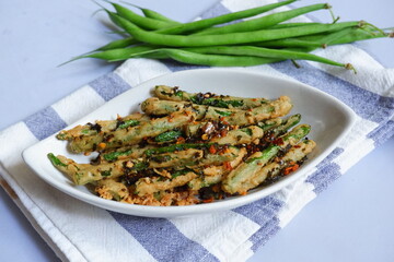 a plate of fried crispy green beans served with chili flakes in white background