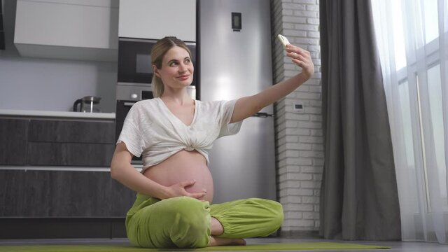 young Caucasian Pregnant woman Takes pictures of herself on her smartphone, Poses, smiles. The concept of pregnancy, technology, preparation and waiting for a child