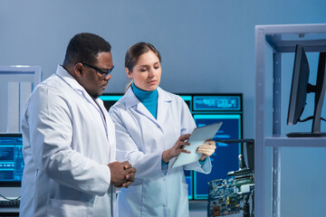 Diverse team of microelectronic engineers discuss current developments in a science lab. Workplace...