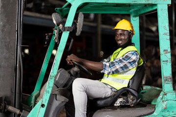 Fototapeta na wymiar African American male driver warehouse worker in safety vest and helmet driving and operating on forklift truck in industry factory. Black worker working at warehouse factory