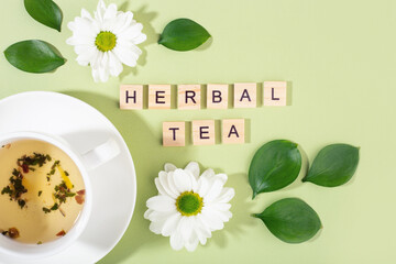 the inscription herbal tea, tea cup, flowers and leaves on green background, hard light