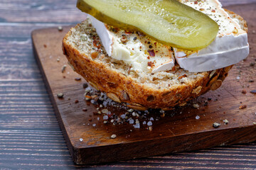 Half a wholemeal roll, topped with two slices of Camembert, one slice of a pickled cucumber and spices.