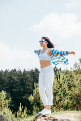 young smiling woman standing on cliff catching wind