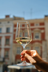 A glass of white wine in the hands of a girl relaxing on restaurant terrace. Summer holiday. Celebrate and enjoy moment. Alcoholic drink tasting. Romantic evening aperitif. Wine glass close up