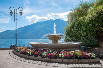 beautiful fountain at lake shore Gardasee, tourist resort Limone with colorful impatiens flowers