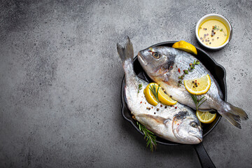 Raw fresh fish sea bream or dorado with lemon, thyme, rosemary and seasonings in cast iron skillet...