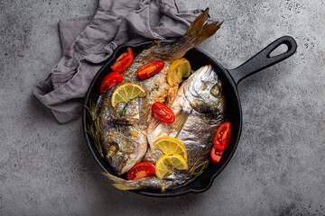 Roasted or fried fresh fish sea bream or dorado with lemon, herbs and tomatoes in cast iron skillet...