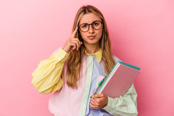 Young caucasian blonde student woman holding books isolated pointing temple with finger, thinking, focused on a task.