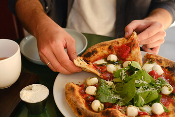 Delicious pizza with cheese tomato and herbs in the hands of a man. Natural products and healthy food. Close-up of a human hand with a slice of italian juicy pizza. Fast food. Lunch time