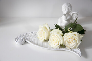 a white faience angel and bunch of roses are on the table.