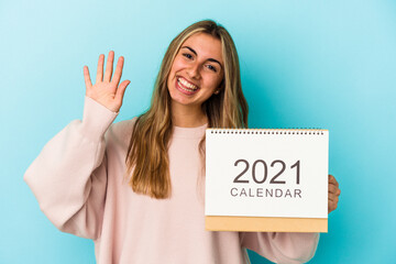 Young blonde caucasian woman holing a calendar isolated smiling cheerful showing number five with fingers.