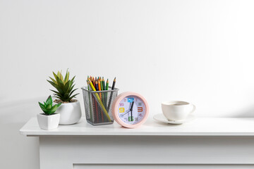Artificial succulent in a ceramic pot, pink alarm clock, pencil holder with pencils on a white table top