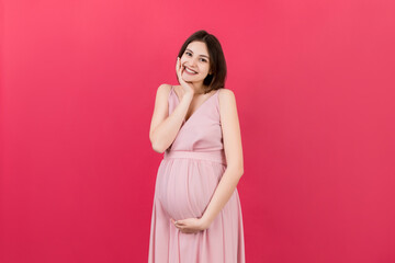 Happy pregnant woman touching her abdomen at Colored background. Future mother is wearing white underwear. Expecting of a baby. Copy space