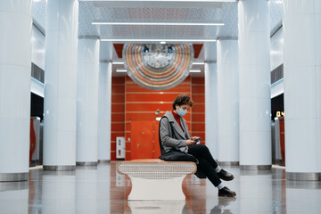 young woman with a smartphone sitting on a bench in the subway.