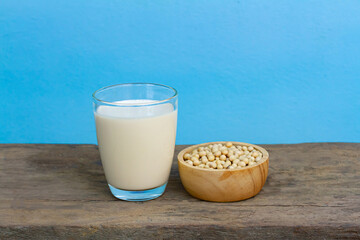 Soy milk in transparent glass with soybeans in wooden bowl on wooden table and blue background....