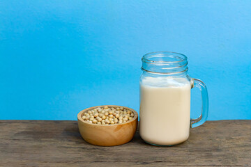 Soy milk in transparent glass with soybeans in wooden bowl on wooden table and blue background. Healthy concept.