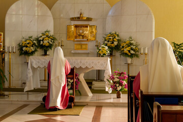 Two nuns dressed in pink and white robes kneeling praying and worshiping the Blessed Sacrament of...