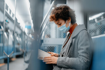 woman in a protective mask reads a book on a subway train.