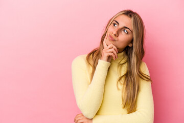 Young blonde caucasian woman isolated on pink background looking sideways with doubtful and...
