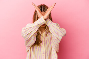 Young blonde caucasian woman isolated on pink background keeping two arms crossed, denial concept.