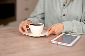woman hands holding coffee cup and white tablet on table