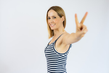Fototapeta na wymiar Beautiful smiling young woman in striped dress showing victory sign isolated over white background.