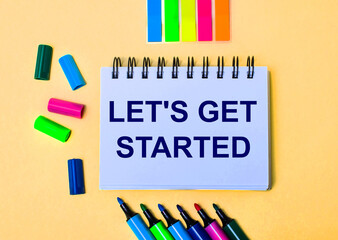 On a beige background, a notebook with the words LET IS GET STARTED, bright felt-tip pens and stickers