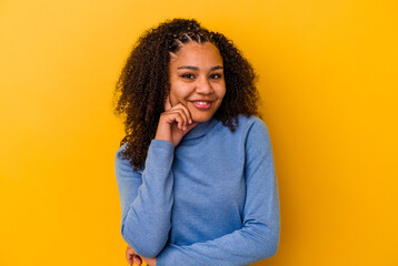 Young african american woman isolated on yellow background smiling happy and confident, touching chin with hand.