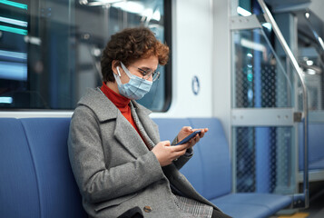 woman in a protective mask reading correspondence sitting in an empty subway car.