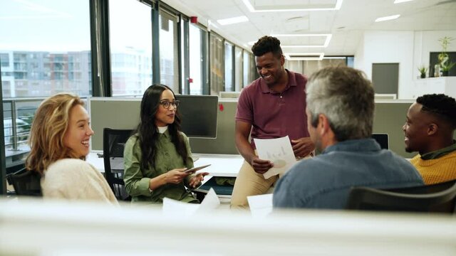 Diverse group of co-workers chatting about upcoming collaboration project holding documents 