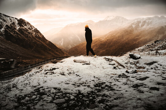 Mann in dunkler Kleidung und gelber M&uuml;tze wandert in den Alpen bei Sonnenaufgang