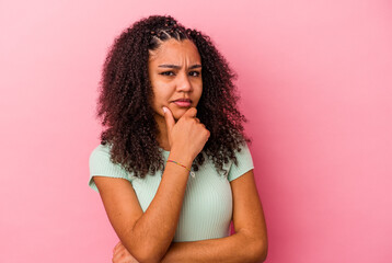 Young african american woman isolated on pink background suspicious, uncertain, examining you.