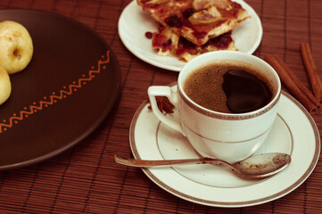 Still life - a hot cup of black coffee, homemade cookies with fruit, baked apples on a bamboo mat