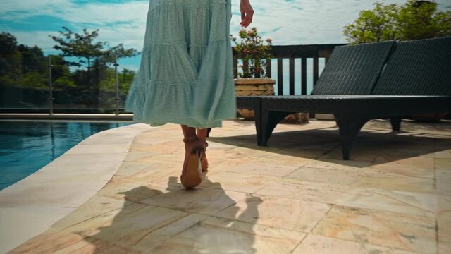 girl walking in the backyard with a green garden, pool with blue clean water and blue sky in a beautiful long blue dress