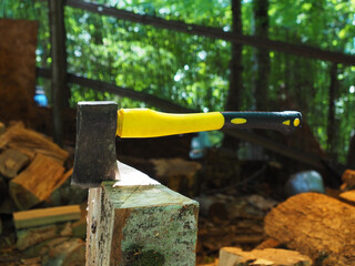 An ax with a yellow handle stuck into a log in a gazebo against a blurred background