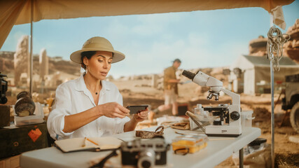 Archaeological Digging Site: Great Female Archaeologist Doing Research, Uses Smartphone to Scan and...
