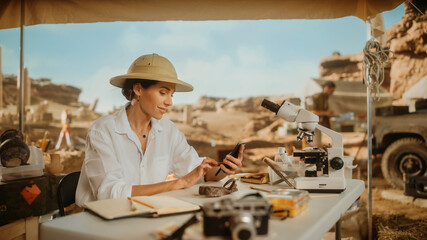 Archaeological Digging Site: Great Female Archaeologist Doing Research, Uses Smartphone to Post...