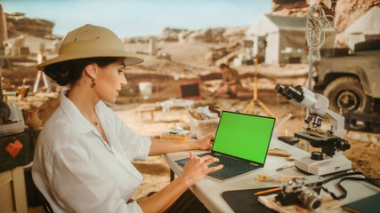 Archaeological Digging Site: Female Archaeologist Using Green Screen Chroma Key Display Laptop, Analysing Fossil Remains, Ancient Civilization Culture Artifacts. Historians work on Excavation Site
