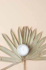 Jar of cosmetic cream with leaf palm branch on pastel beige background. Flat lay, copy space