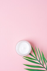 Obraz na płótnie Canvas Jar of cosmetic cream with leaf palm branch on pink background. Flat lay, copy space