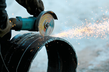 The angle grinder cuts a large-diameter metal pipe and sparks fly. Close-up of work in production.