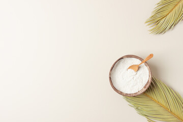 Collagen powder in bowl with measure spoon with palm leaves on pastel beige background. Flat lay, copy space