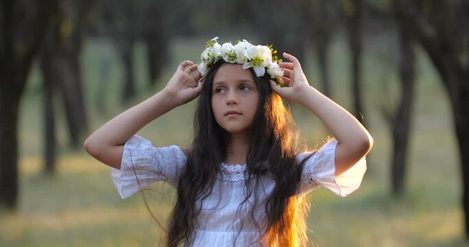 Portrait of a  Caucasian teenager girl with long brown hair and blue eyes in a flower wreath dancing and smelling bouquet of flowers on a nature background. 4k 50 fps slow motion