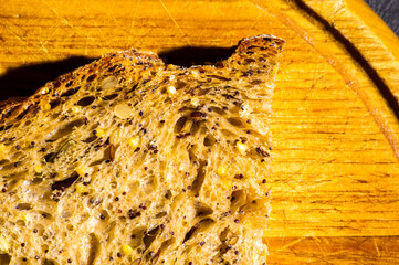 Slice of rustic natural yeast-free bread with flax, poppy seeds, sesame seeds, millet, pumpkin and sunflower seeds, on a wooden board, black background, hard light, photo in a low key, close up.