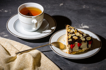 Still life - layered homemade sponge cake and a cup of black tea in a white dish, and a linen napkin, black background, hard light, photo in a low key.