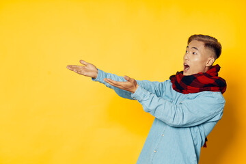 a man in a blue shirt with a scarf around his neck shows with his hands to the side on a yellow background