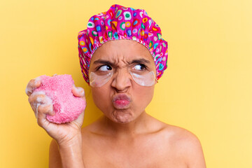 Young mixed race woman with shower cap holding a sponge isolated on yellow background